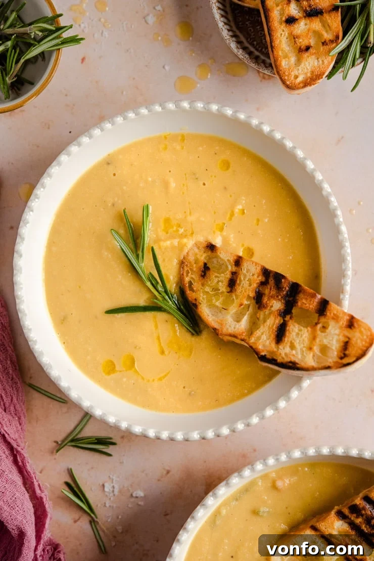 An overhead shot of chickpea soup in a bowl topped with a sprig of rosemary, emphasizing its appetizing presentation.