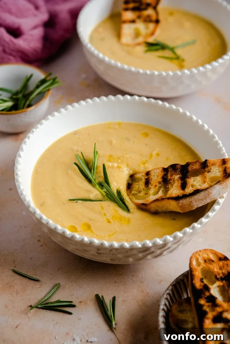 A side shot of chickpea soup in a bowl topped with crusty bread, showing the appealing texture and garnishes.