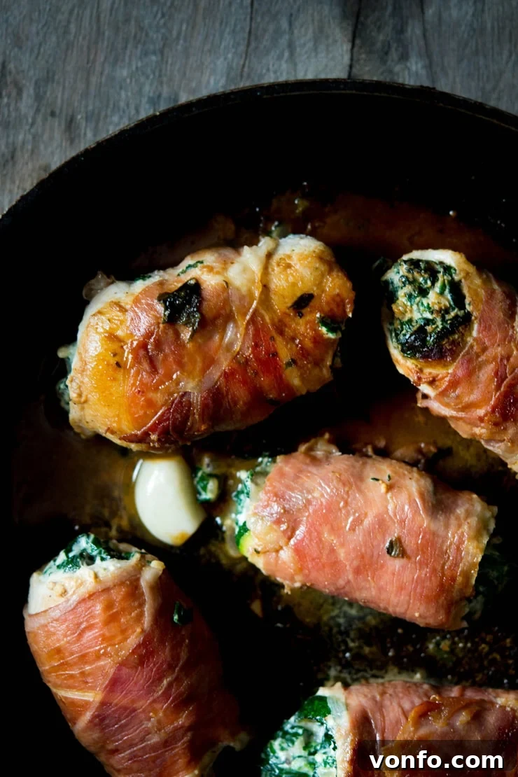 A close up photo of the cooked chicken involtini in a pan, showcasing the golden-brown prosciutto and the creamy spinach and ricotta filling peeking out.