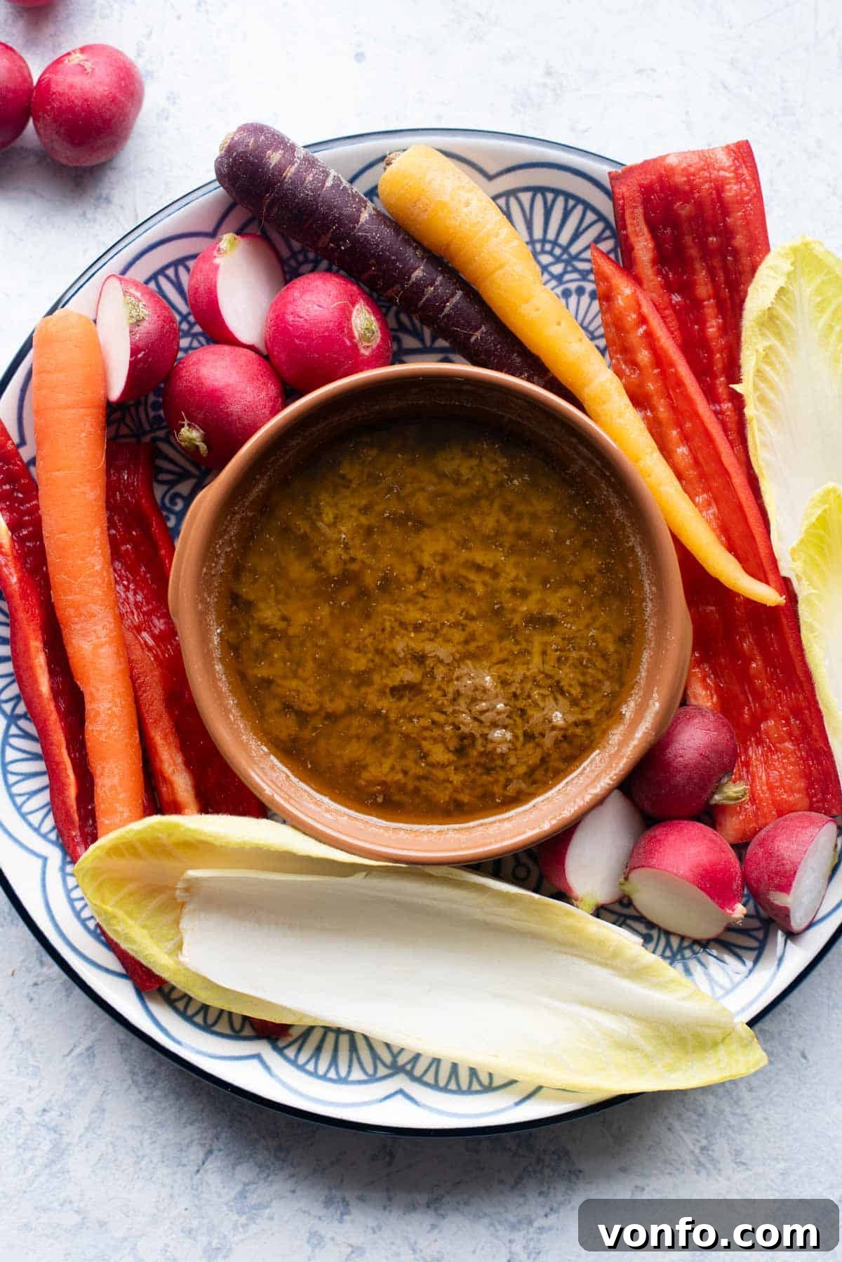 Bagna Cauda: The Ultimate Warm Garlic and Anchovy Butter 2 An overhead shot of Bagna Cauda in a terracotta dish with a vibrant selection of raw seasonal vegetables like carrots, radicchio, and celery arranged around it, ready for dipping.