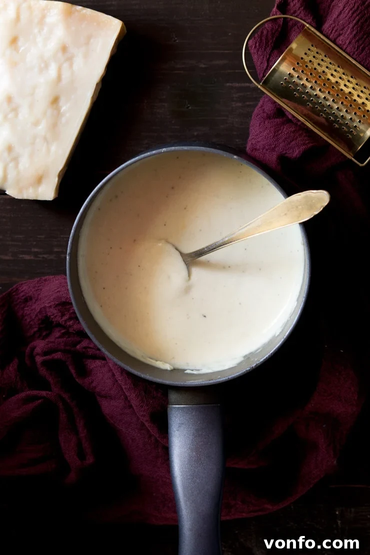 Overhead shot of white sauce in a saucepan with a spoon in it - how to make bechamel sauce recipe (no butter)