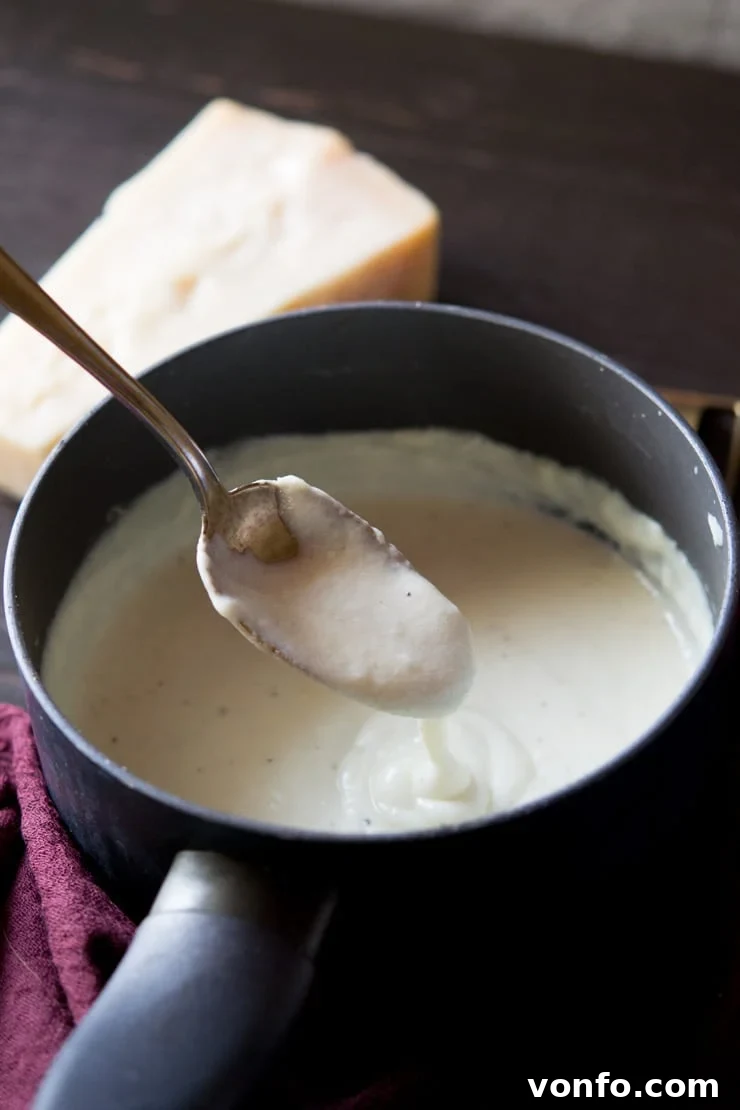 A close up shot of bechamel sauce in a saucepan with parmesan in background - how to make bechamel sauce recipe
