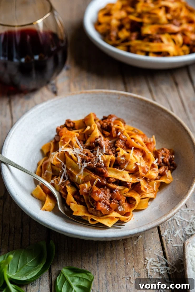 Authentic Italian Beef Ragu Recipe Rich Italian beef ragu generously tossed with fresh tagliatelle pasta in a rustic white bowl, garnished with vibrant fresh parsley and a dusting of grated Parmesan cheese.