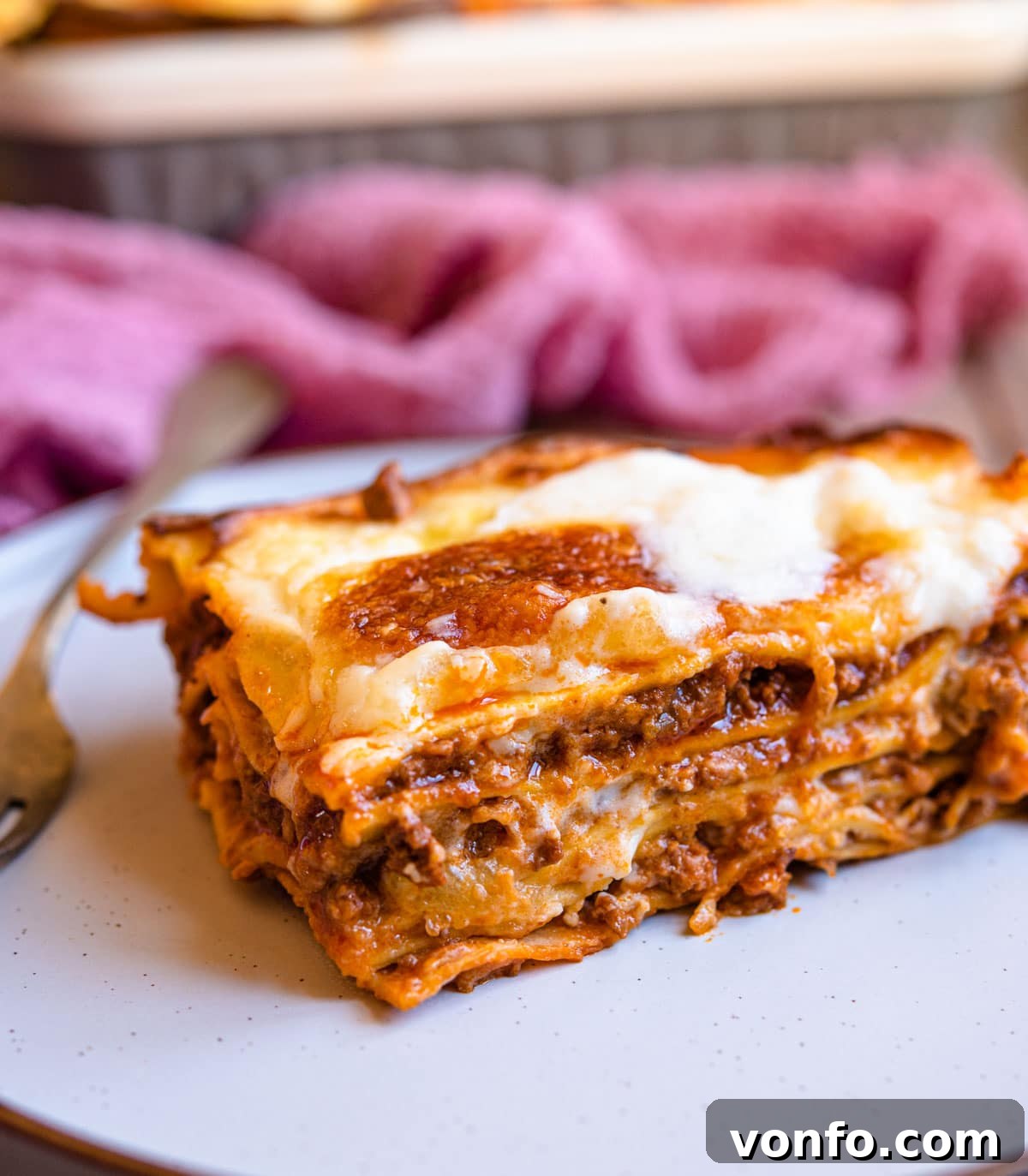 A close up of a perfectly golden slice of lasagne al forno on a white plate, showing the distinct layers