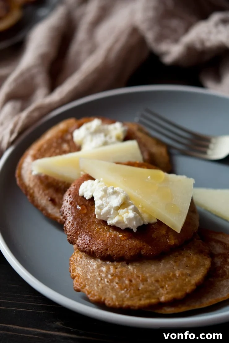 Close-up of Chestnut Fritters with Toppings A close-up view of a chestnut fritter, showcasing its golden-brown, crispy exterior and being topped generously with creamy ricotta cheese, delicate shavings of pecorino, and a shimmering drizzle of golden truffle honey.