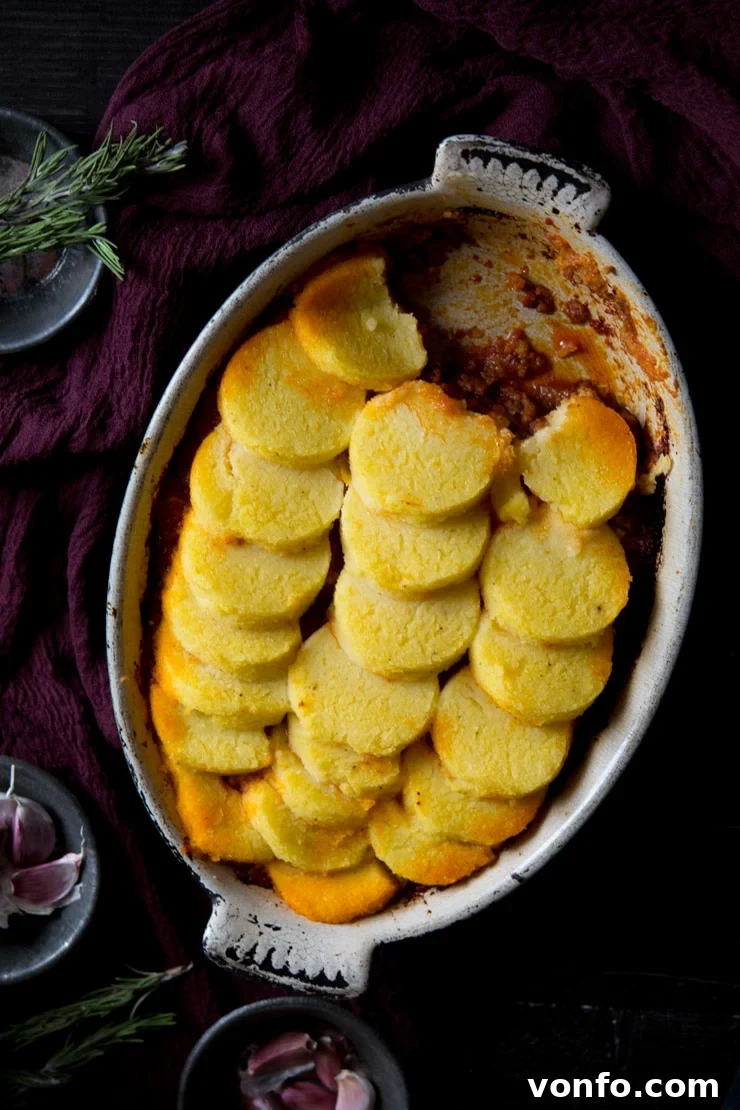 Baked Polenta with Beef and Sausage Ragu, ready for serving A large oval baking dish filled with rich beef and sausage ragu, topped generously with golden-baked polenta rounds, garnished with fresh parsley.