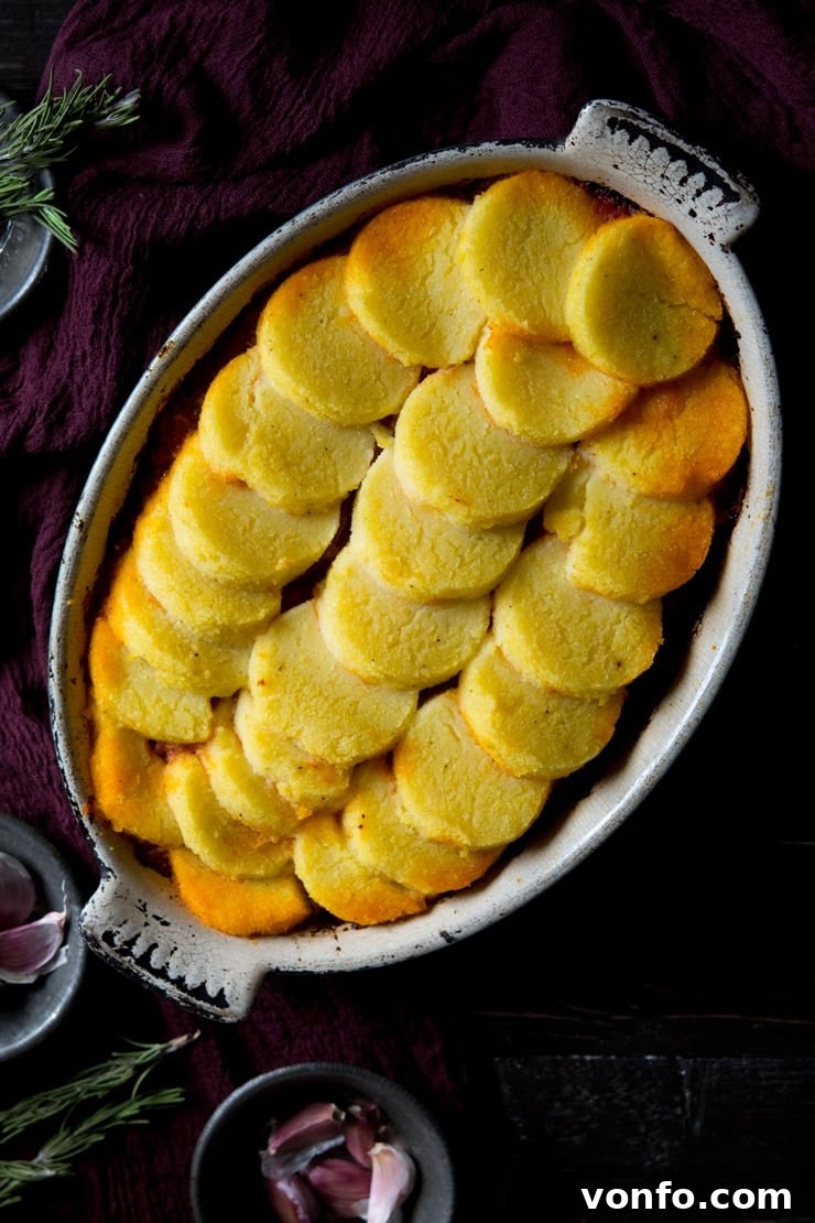 A delicious view of the Baked Polenta with Beef and Sausage Ragu A close-up of the Baked Polenta with Beef and Sausage Ragu in a baking dish, showcasing the bubbling ragu beneath golden, crispy polenta and fresh herb garnish.