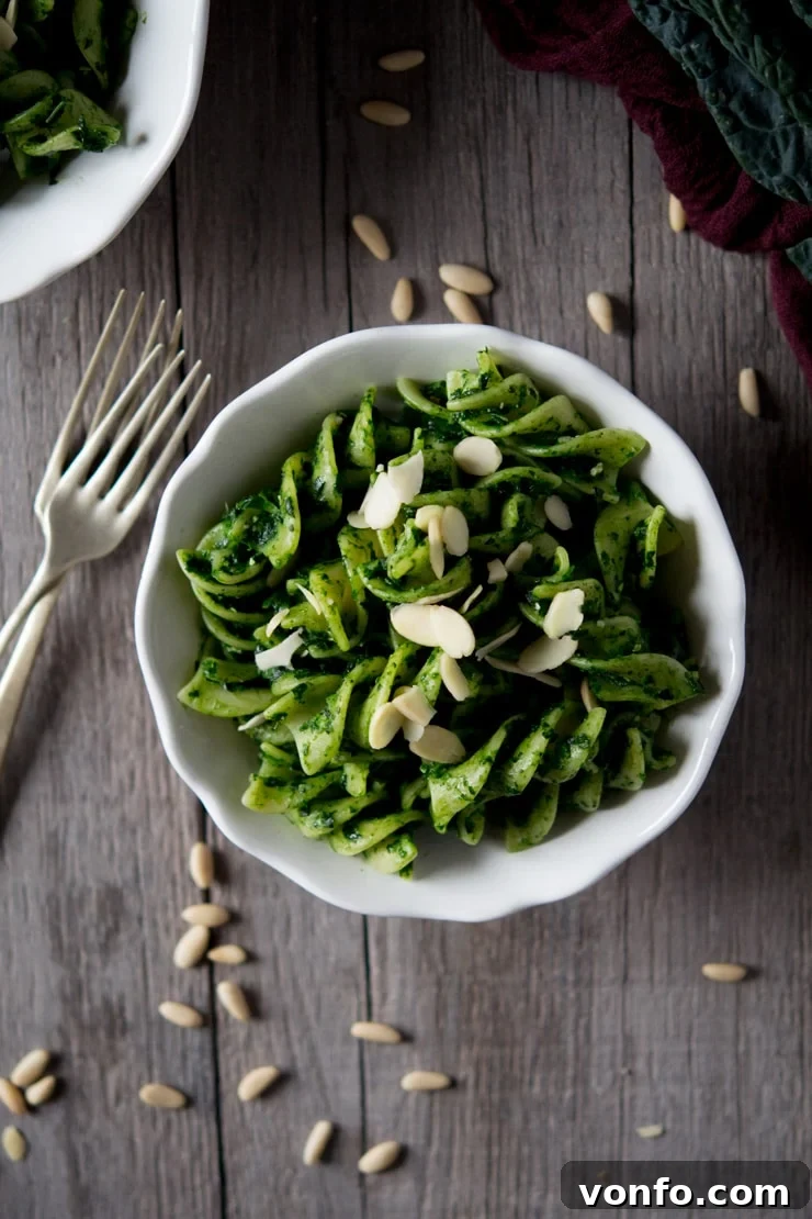 Healthy Cavolo Nero Pesto Pasta Vibrant green cavolo nero pesto pasta served in a white bowl on a rustic wooden table, garnished with flaked almonds and a fork
