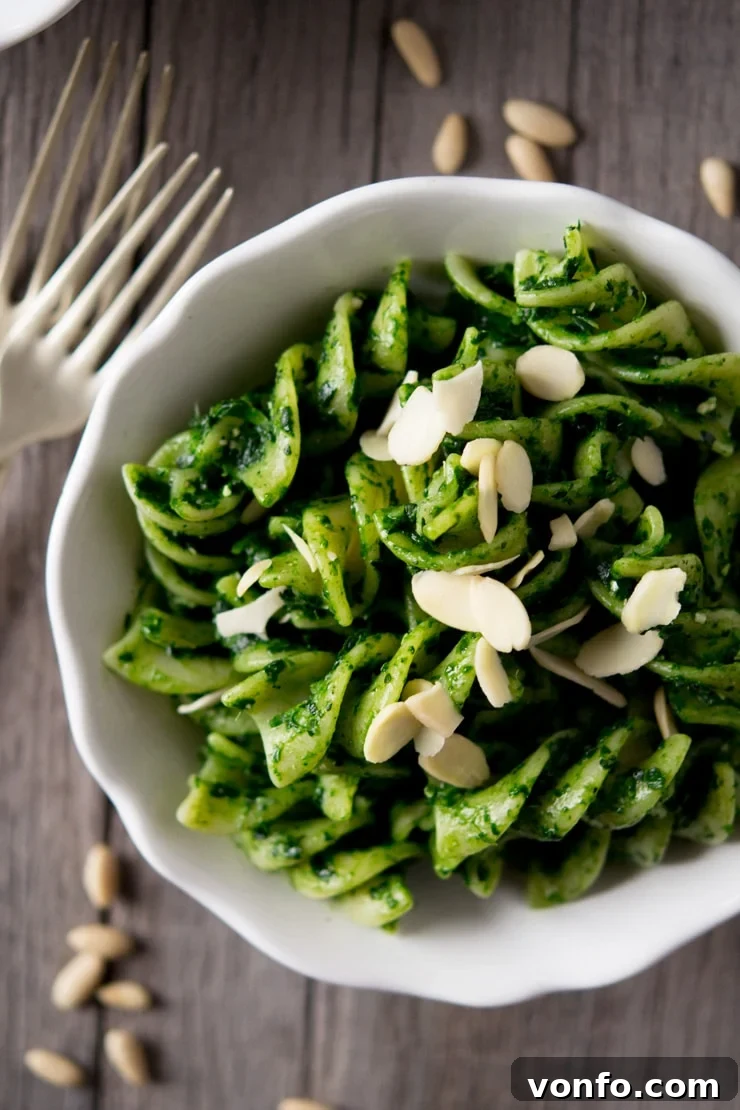 Delicious Cavolo Nero Pesto Pasta Up Close Close-up view of a serving of healthy cavolo nero pesto pasta, featuring plump fusilli generously coated in verdant sauce and topped with crunchy flaked almonds, presented in a white bowl
