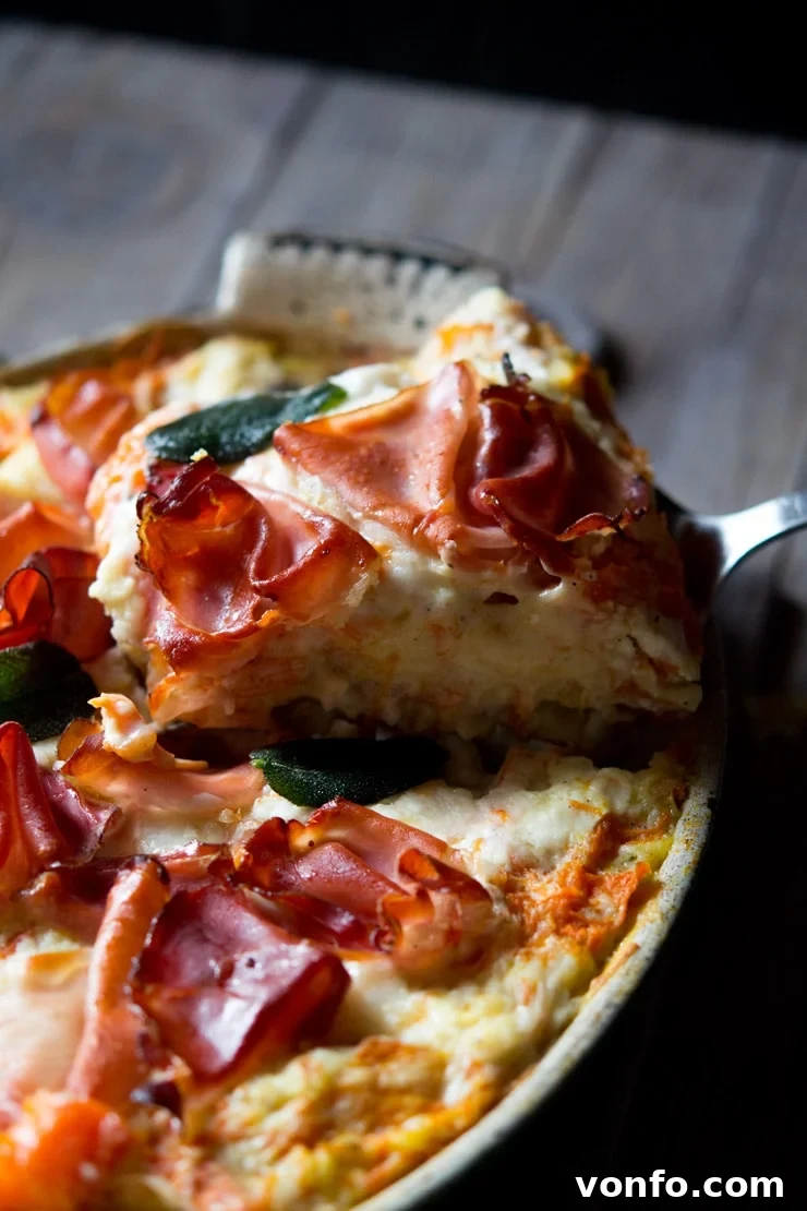 A close up shot of a slice of butternut squash lasagna topped with prosciutto, served on a white plate