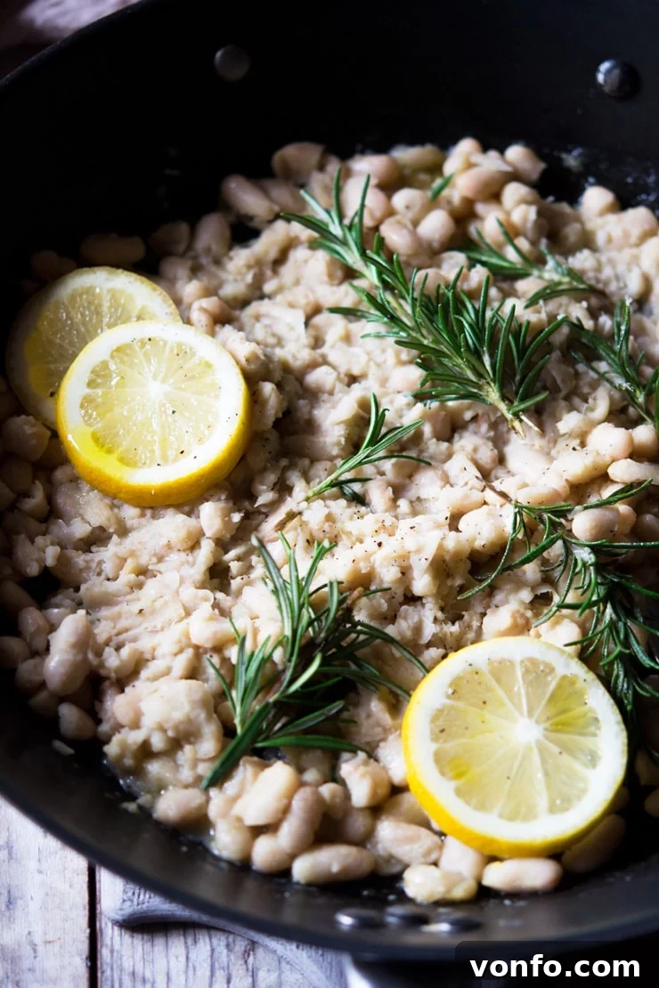 Close-Up of White Bean Mash with Rosemary and Lemon Garnish A close up of cannellini bean mash topped with sprigs of rosemary and slices of lemon in a large pan