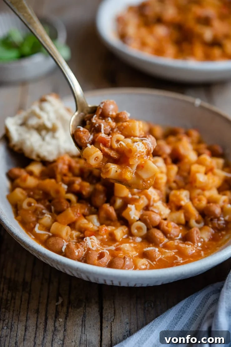 A close-up shot of a spoon scooping up rich, thick pasta fagioli soup, highlighting the tender beans and small pasta shapes.
