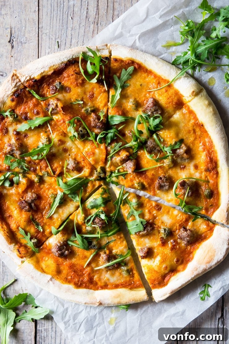 An overhead shot of pizza with sausage, roasted red pepper sauce, mozzarella and arugula sitting on a wooden surface An overhead shot of pizza with sausage, roasted red pepper sauce, mozzarella and arugula sitting on a wooden surface