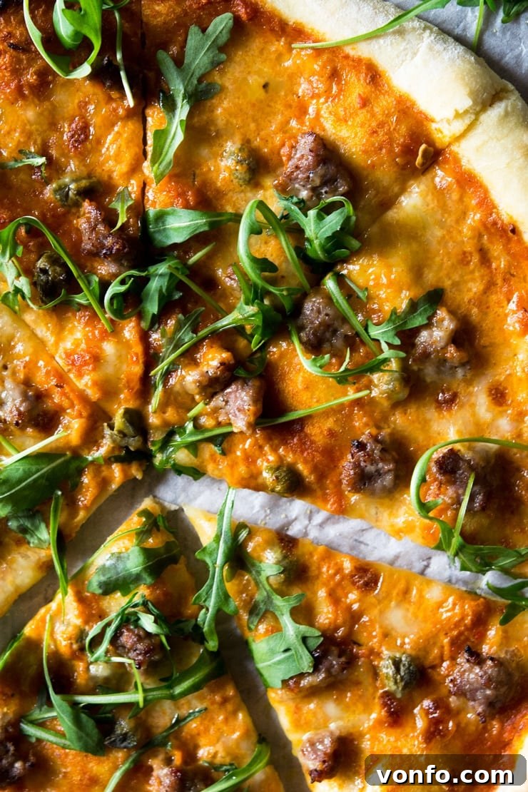A close up of pizza with sausage and roasted red pepper sauce, melted mozzarella and topped with arugula. A close up of pizza with sausage and roasted red pepper sauce, melted mozzarella and topped with arugula.