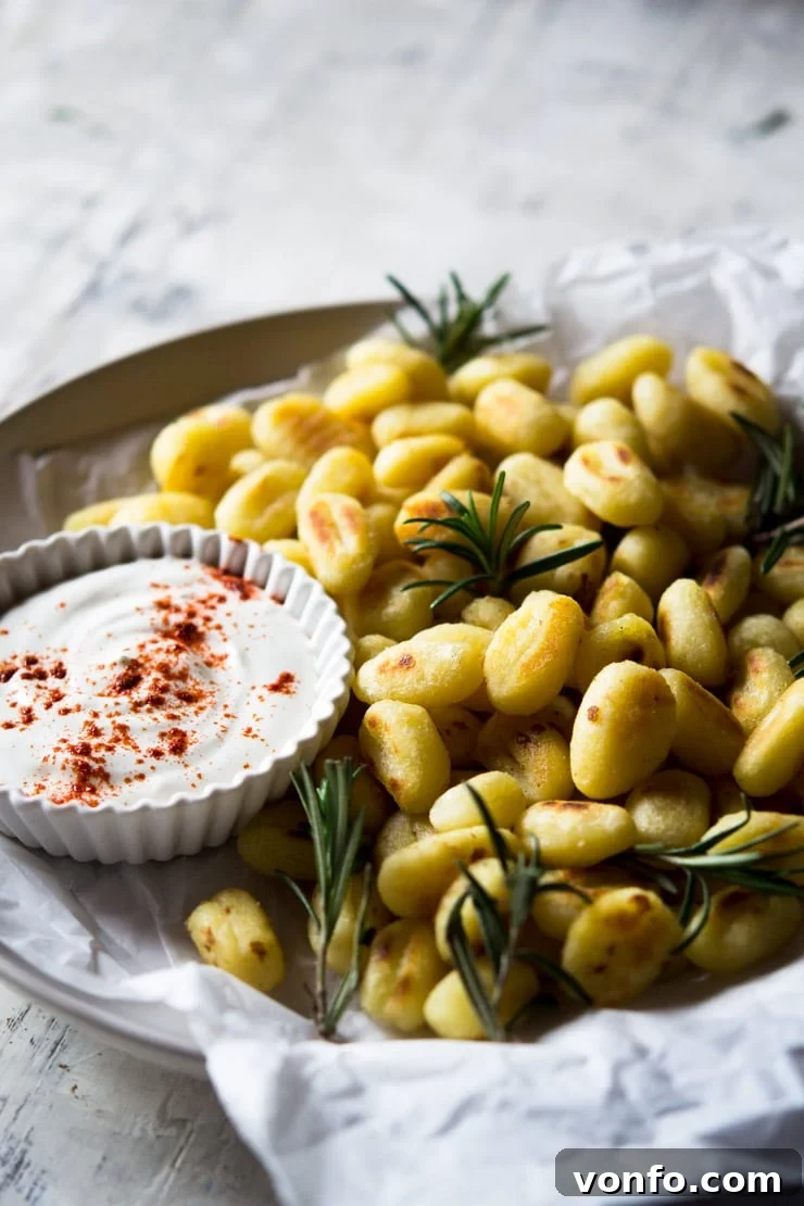 Close-Up of Crispy Gnocchi with Rosemary and Dip A close up of fried gnocchi on a plate with rosemary and a sour cream dip