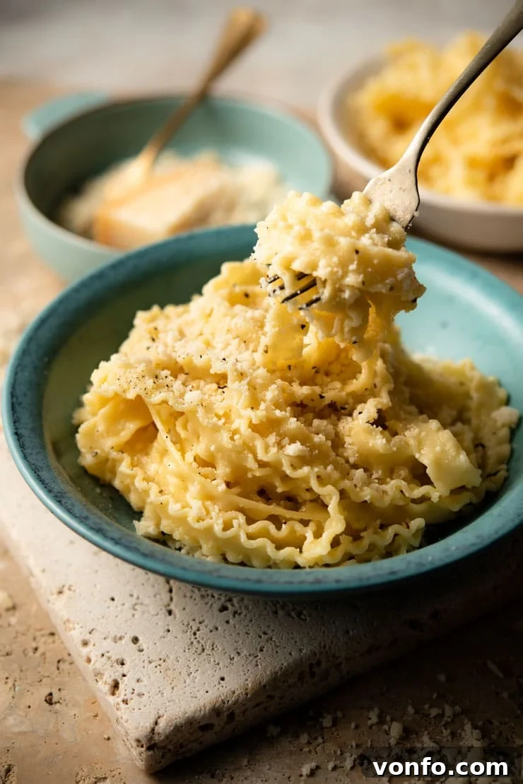 A fork picking up some parmesan pasta from a bowl, highlighting the cheesy strands and coarse grated cheese.