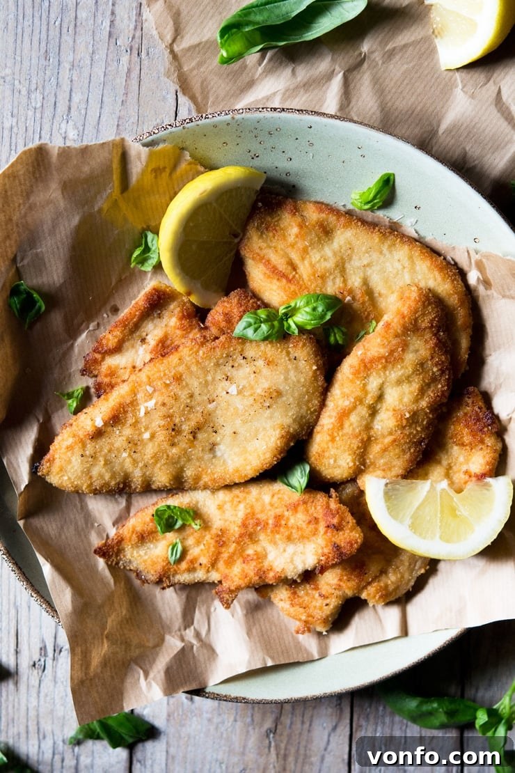 Crispy Fried Chicken Cutlets An overhead shot of freshly fried, golden-brown breaded chicken cutlets neatly arranged on a piece of brown parchment paper, highlighting their perfect crispiness.