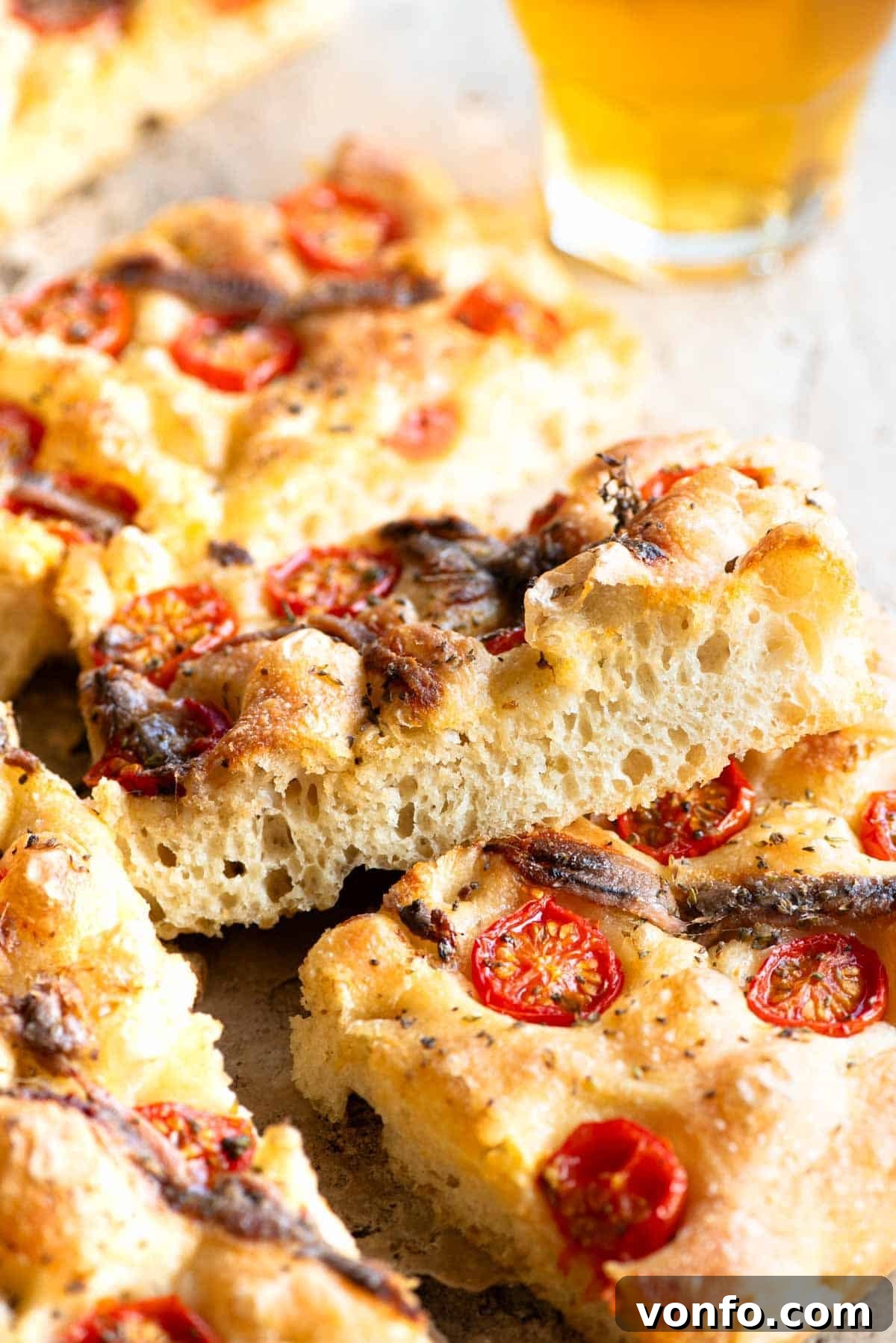 Coastal Focaccia with Bursting Cherry Tomatoes, Salty Anchovies, and Aromatic Oregano 7 A close up of a slice of tomato and anchovy focaccia on its side showing the airy and bubbly texture inside, emphasizing the perfect crumb.