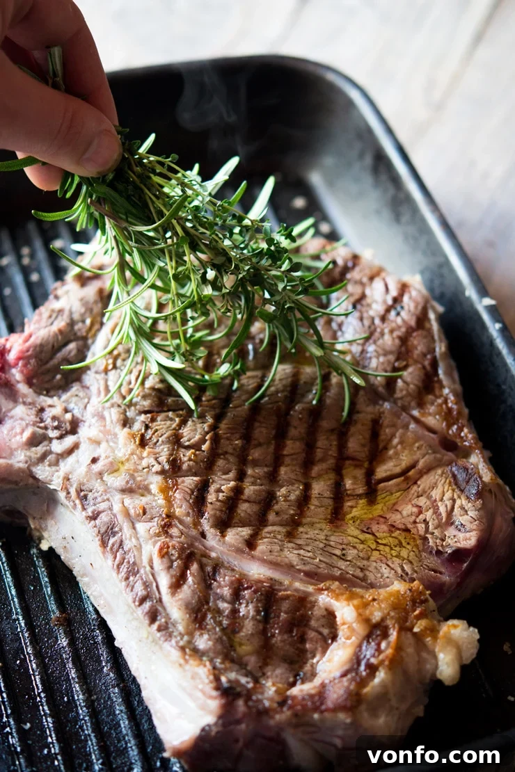 Herbs Applied to Florentine Steak A hand gently brushing fresh rosemary and thyme herbs over a sizzling Florentine steak on a griddle, adding subtle flavor during cooking.