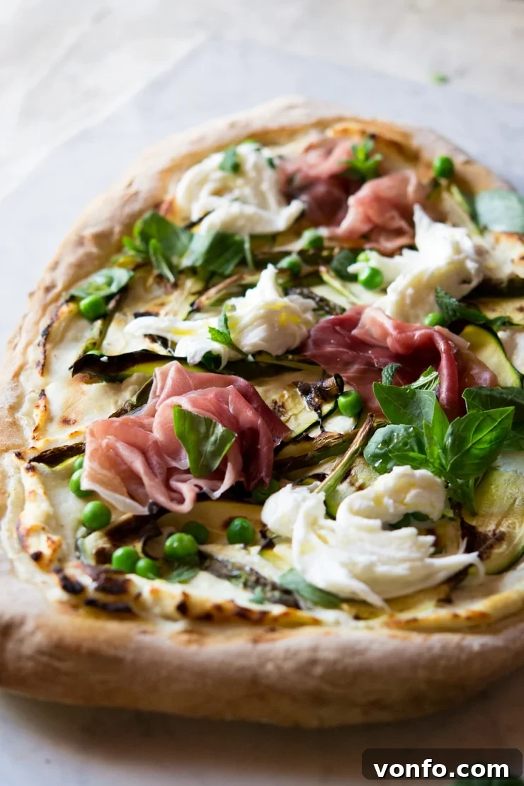 Close-Up: Zucchini, Prosciutto, Asparagus Pizza A close-up shot of the finished white pizza, showing the detailed textures of zucchini ribbons, prosciutto slices, asparagus, melted buffalo mozzarella, and fresh herbs.
