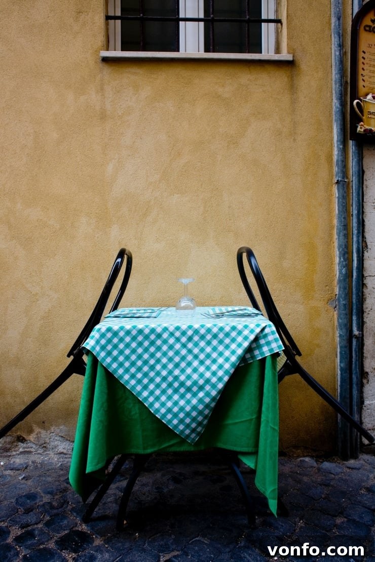 A photo of a yellow outside wall of a building with a table with a green checkered tablecloth and two back seats A photo of a warm yellow building exterior with a rustic table adorned with a green checkered tablecloth and two welcoming chairs, evoking a cozy Italian outdoor dining scene.