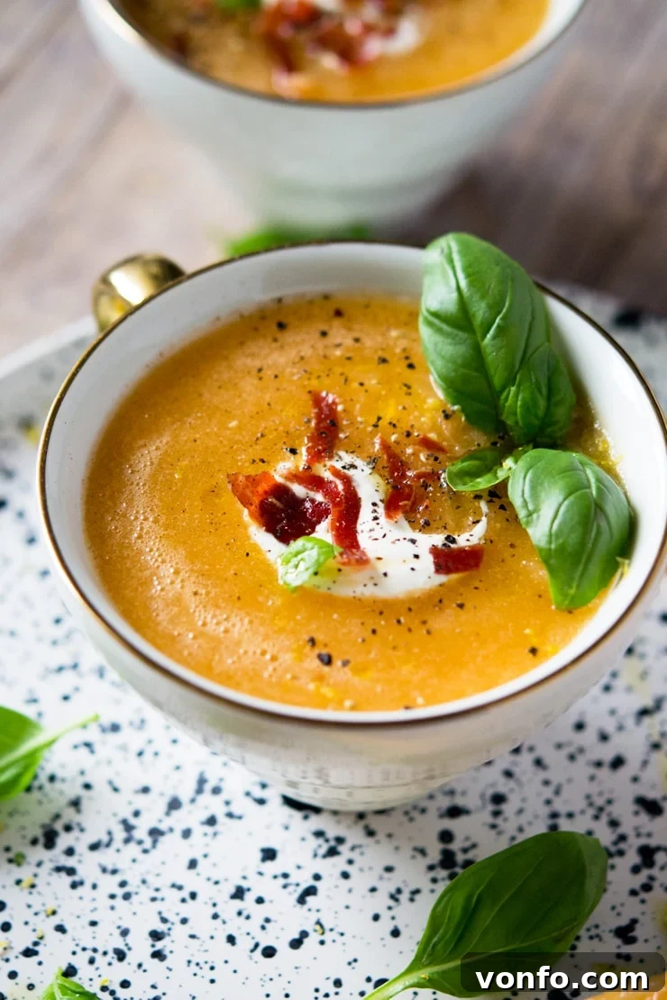 Garnished Melon Gazpacho Ready to Serve A close-up of melon gazpacho soup in a mug topped with a generous dollop of creme fraiche, crumbled crispy prosciutto, and a sprinkle of fresh pepper