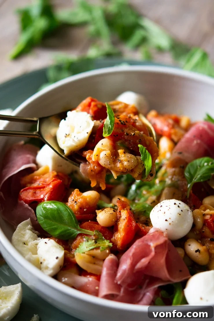 A close up shot of a warm white bean salad with tomato and fresh basil on a serving spoon, highlighting the texture and vibrant fresh ingredients