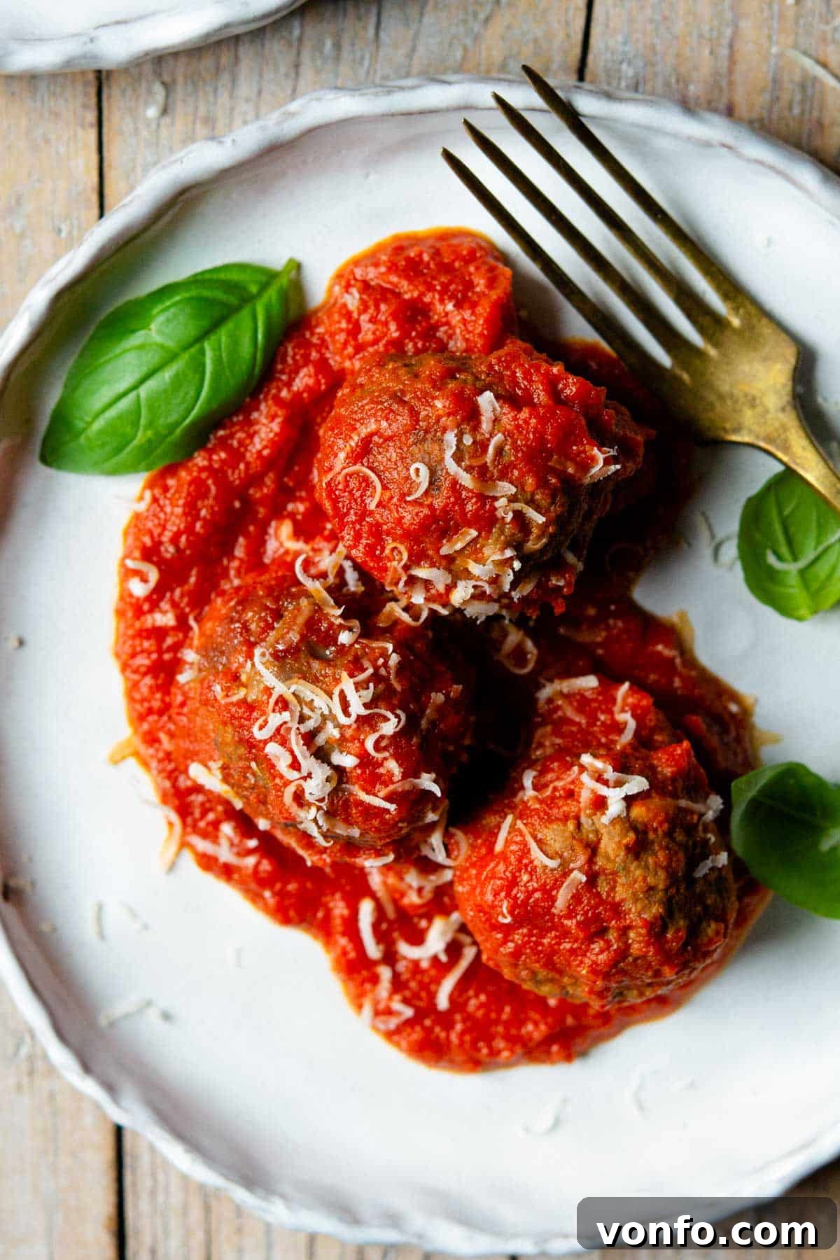 Slow-Cooked Italian Meatballs in Rustic Tomato Sauce 4 An overhead close up of three Italian meatballs on a plate with tomato sauce and basil leaves