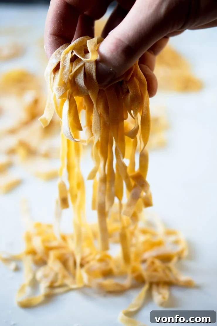 Perfect Homemade Tagliatelle: Fresh Pasta Ready for Your Favorite Italian Sauce A close-up shot of a hand gently holding a beautifully formed bundle of freshly made tagliatelle, showcasing the exquisite golden color and silky smooth texture of the homemade pasta dough. The strands are perfectly cut and ready to be cooked and enjoyed, embodying the freshness and quality of traditional Italian pasta making.