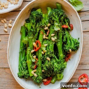 A square image of sautéed broccolini with pesto, pine nuts, and chili, ready for serving