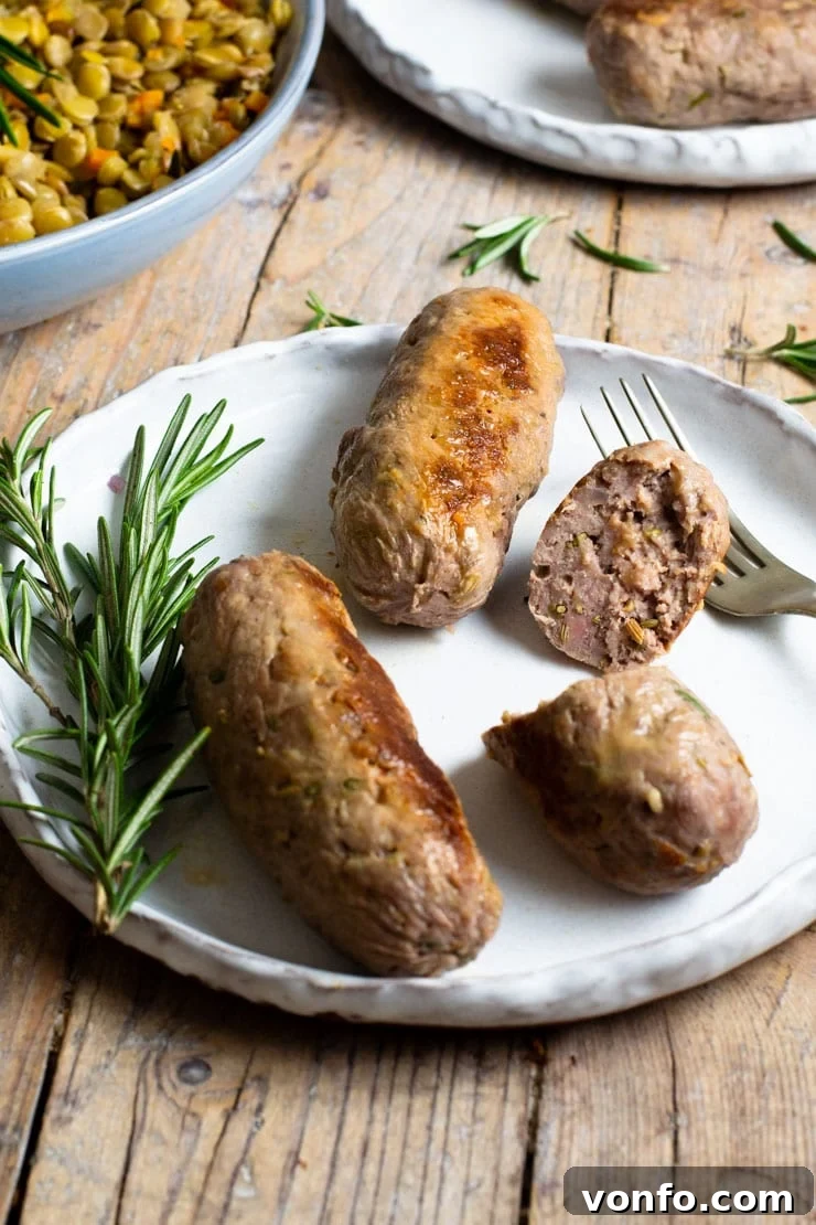 Cooked Homemade Italian Sausage Two perfectly cooked homemade Italian sausages on a plate, one cut in half to reveal its juicy interior. A sprig of fresh rosemary adds a fragrant garnish.