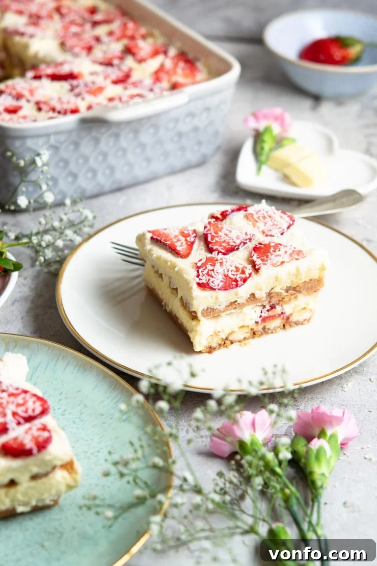 Light, creamy and delicious Strawberry Tiramisu made with juicy strawberries, Cointreau liqueur, and shavings of white chocolate. It's a fresh and summery spin on the classic Italian dessert that's just as delicious and easy to make. #tiramisu #strawberrydessert #Italiandessert A slice of strawberry tiramisu on a white plate with fresh flowers scattered around, showcasing the layers.
