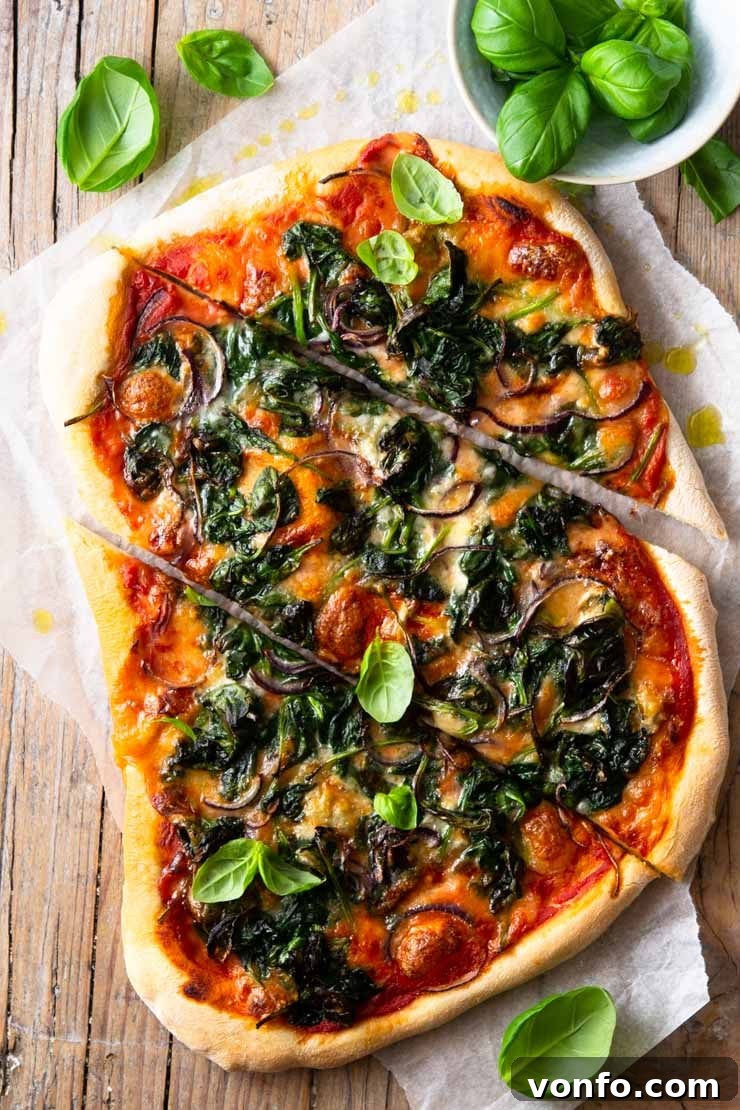 Homemade Spinach Pizza with Gorgonzola, Red Onion & Mozzarella: A Light, Fluffy, Crispy Base with Wilted Spinach An overhead shot of a freshly baked Spinach Pizza cut into slices with basil scattered around, highlighting the melted Gorgonzola and mozzarella cheese, vibrant wilted spinach, and thinly sliced red onion.