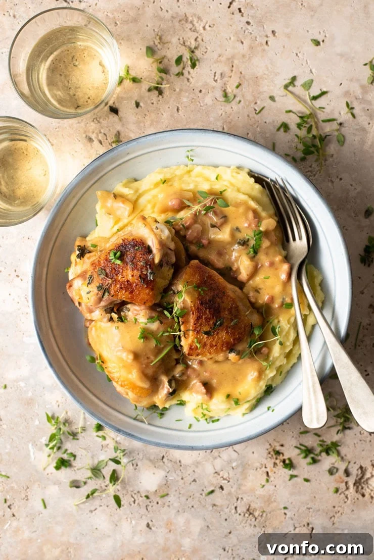 Healthy Creamy Tuscan Chicken with Pancetta and Garlic An overhead shot of creamy Tuscan chicken in a blue bowl with mashed potatoes and glasses of white wine