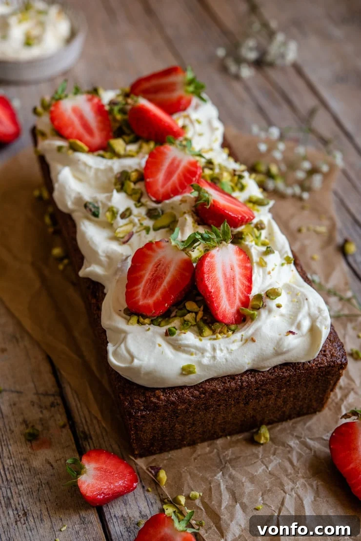 Pistachio Cake with Whipped Cream & Strawberries A side shot of a vibrant pistachio cake generously topped with fresh whipped cream and juicy strawberries, presented on a light plate.