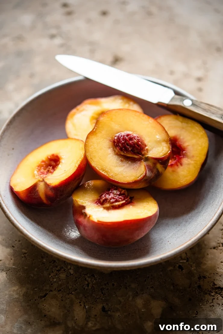 Fresh, perfectly ripe peaches in a bowl, accompanied by a knife, indicating they are ready for preparation to be turned into a delicious puree for Peach Bellini cocktails.