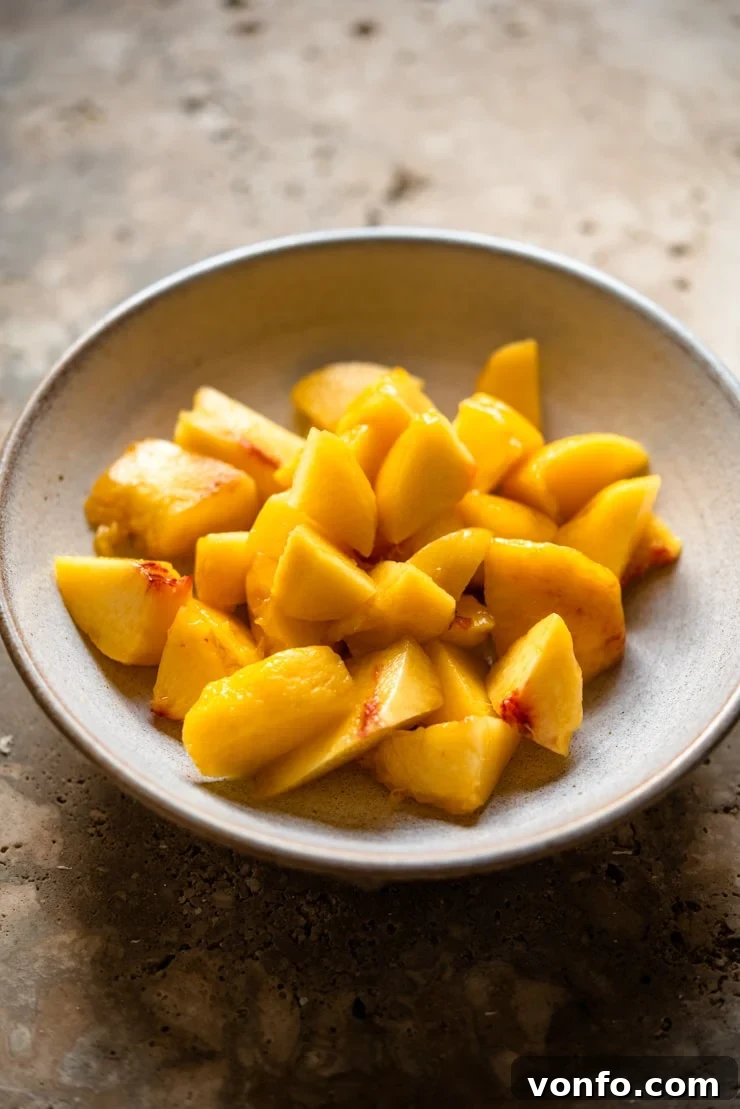 Roughly chopped fresh peaches neatly arranged in a bowl, prepared for blending into a smooth puree for a classic Peach Bellini.