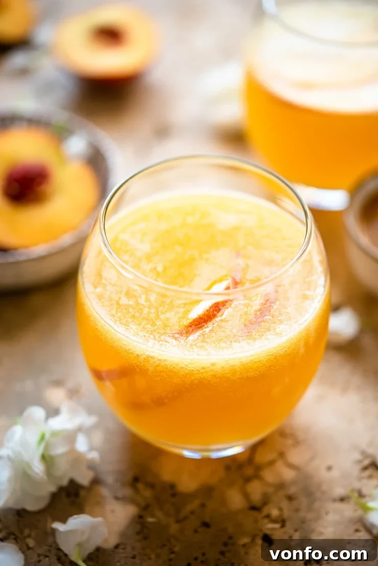 A refreshing Peach Bellini cocktail served in a contemporary round glass, showcasing its vibrant color and inviting bubbles, ready to be enjoyed.