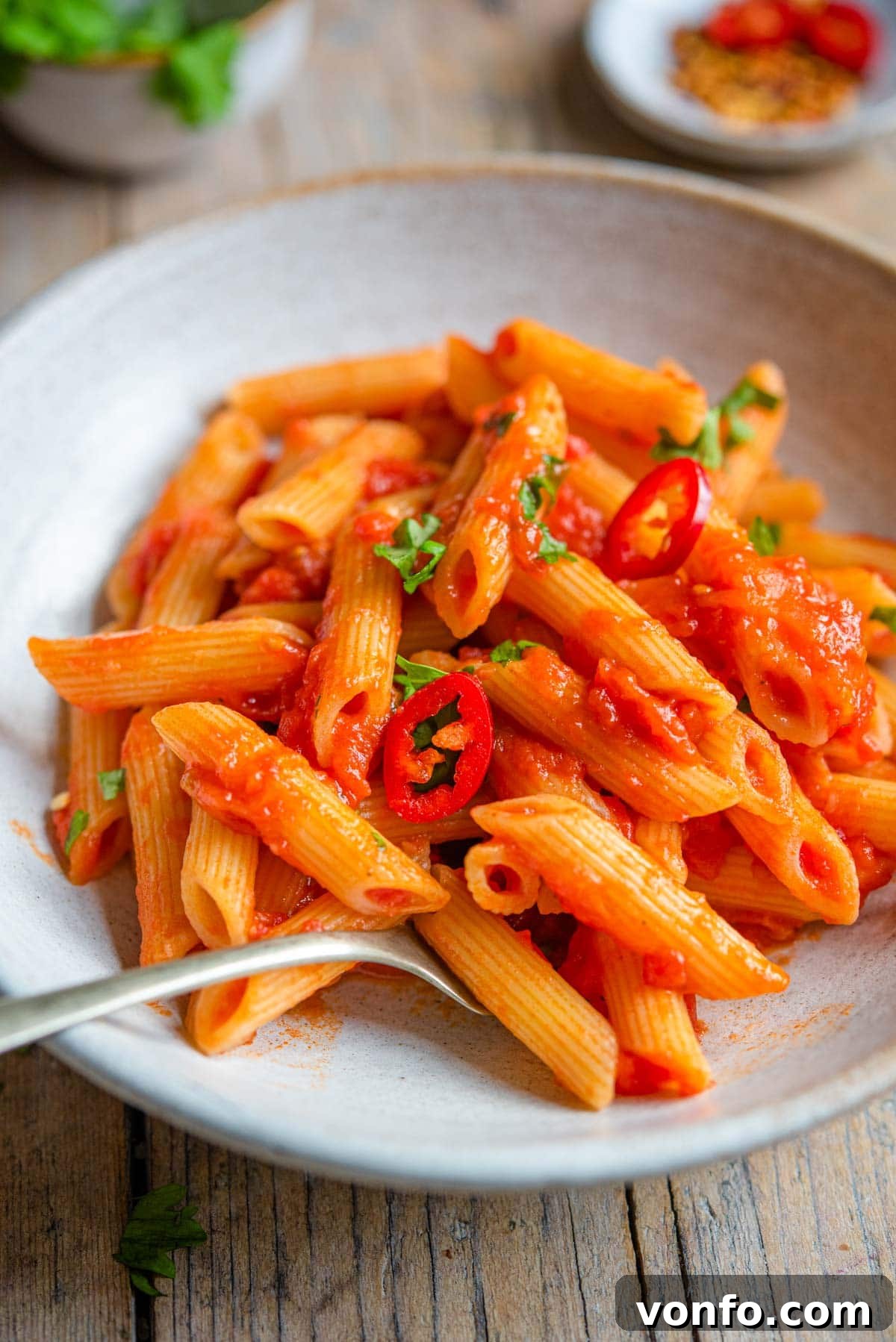 A close up of penne arrabbiata in a rustic bowl with a fork, ready to be eaten