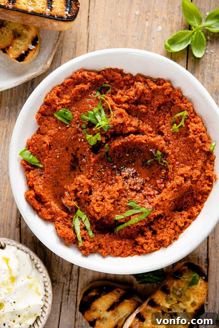 Simple Sun-Kissed Tomato Pesto 4 Red pesto in a small white bowl with fresh basil leaves and crusty bread on a wooden board