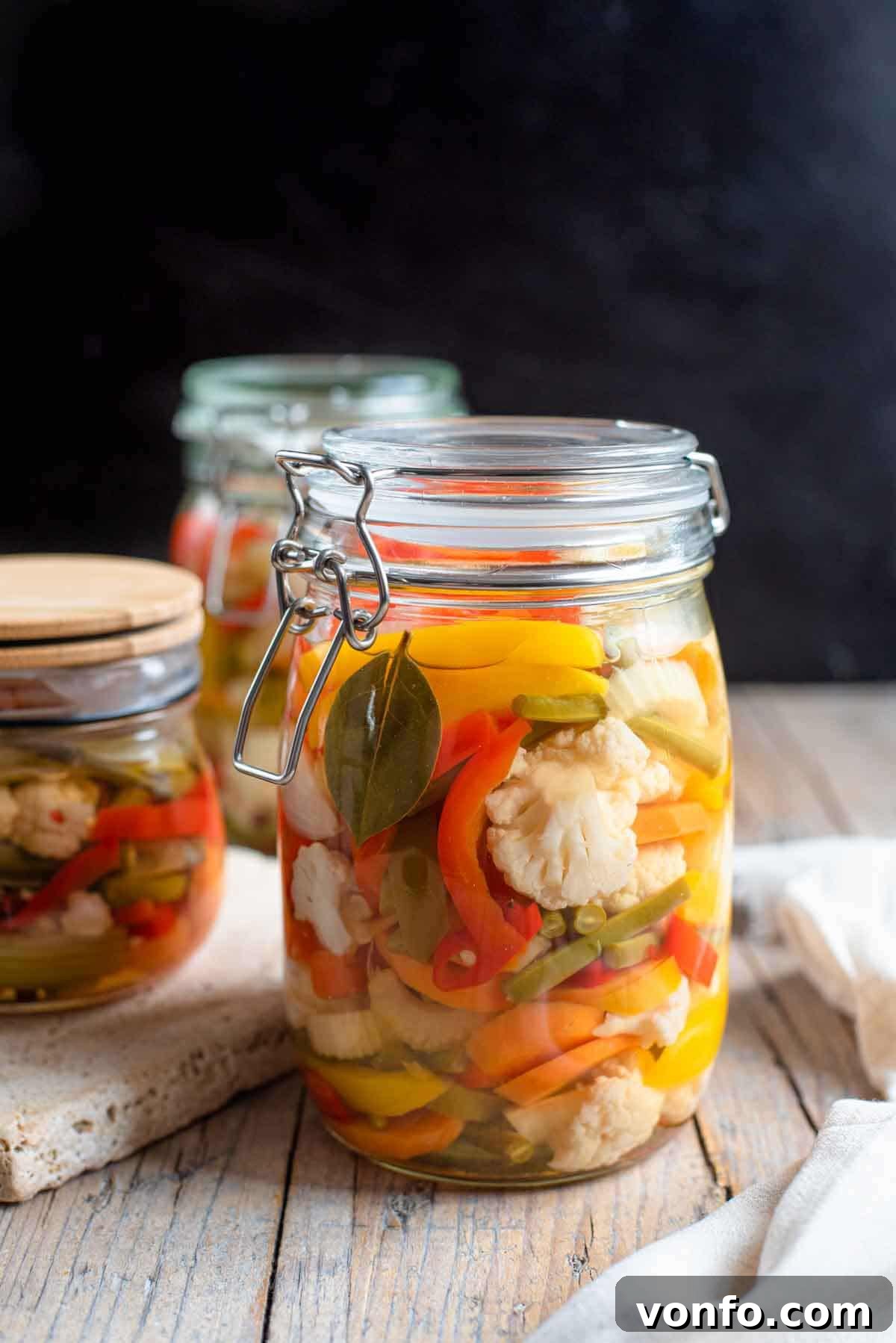 A close up of Giardiniera pickled vegetables in a glass jar, showcasing colorful carrots, cauliflower, and peppers