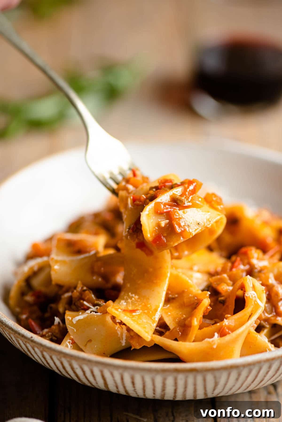 A close-up shot of a fork twirling pappardelle pasta generously coated in rich vegetable ragu and topped with cheese