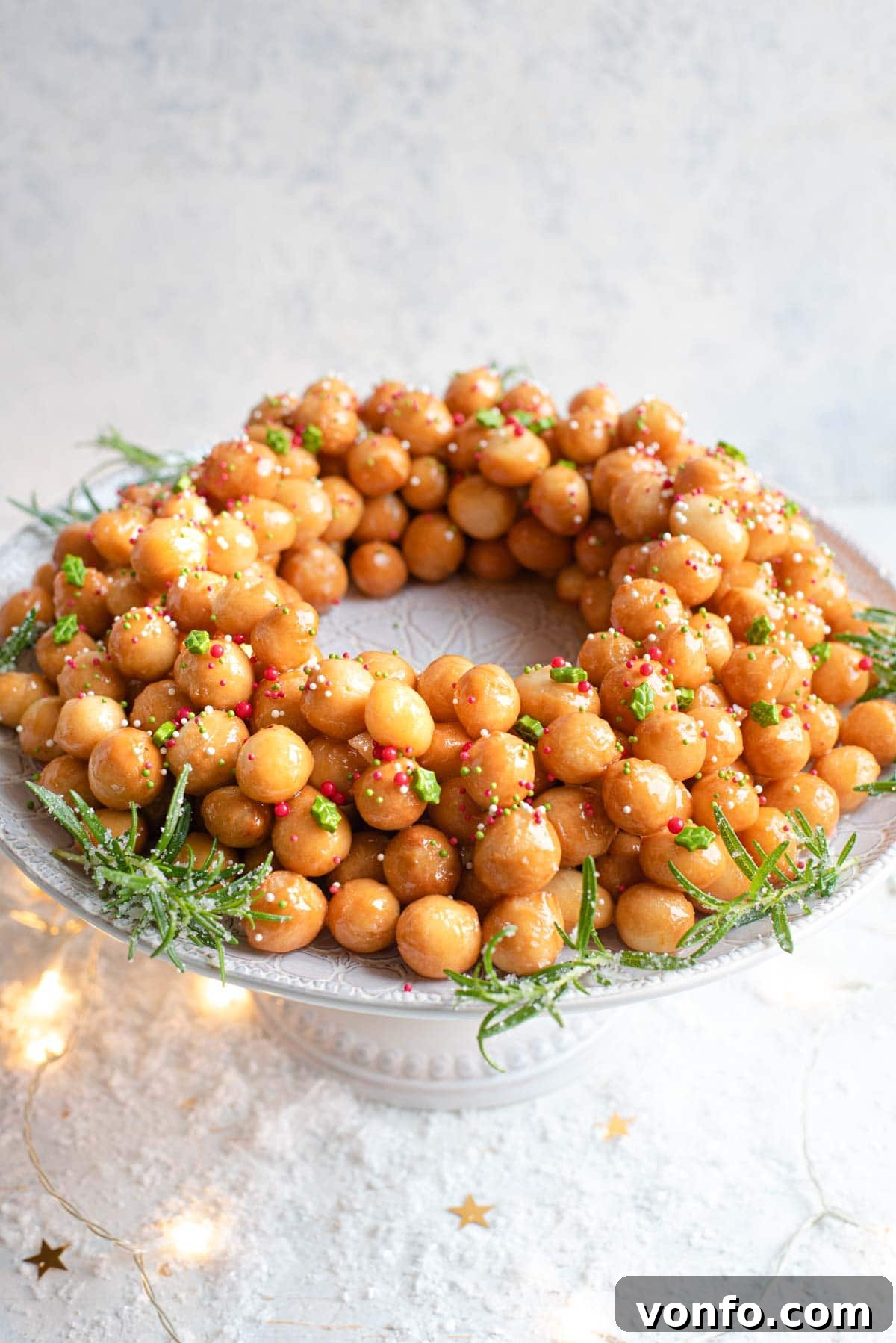 Struffoli Italy's Golden Honey Treats 2 A side shot of a perfectly arranged mound of golden-brown Italian struffoli (honey balls) on a white cake stand, glistening with honey and topped with vibrant festive sprinkles.