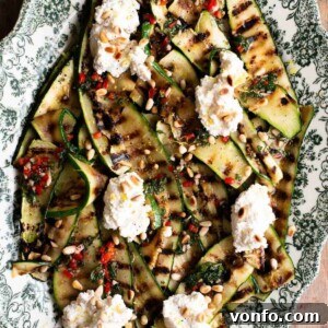 A close up of grilled zucchini on a serving plate topped with mint, chilli and fresh ricotta.