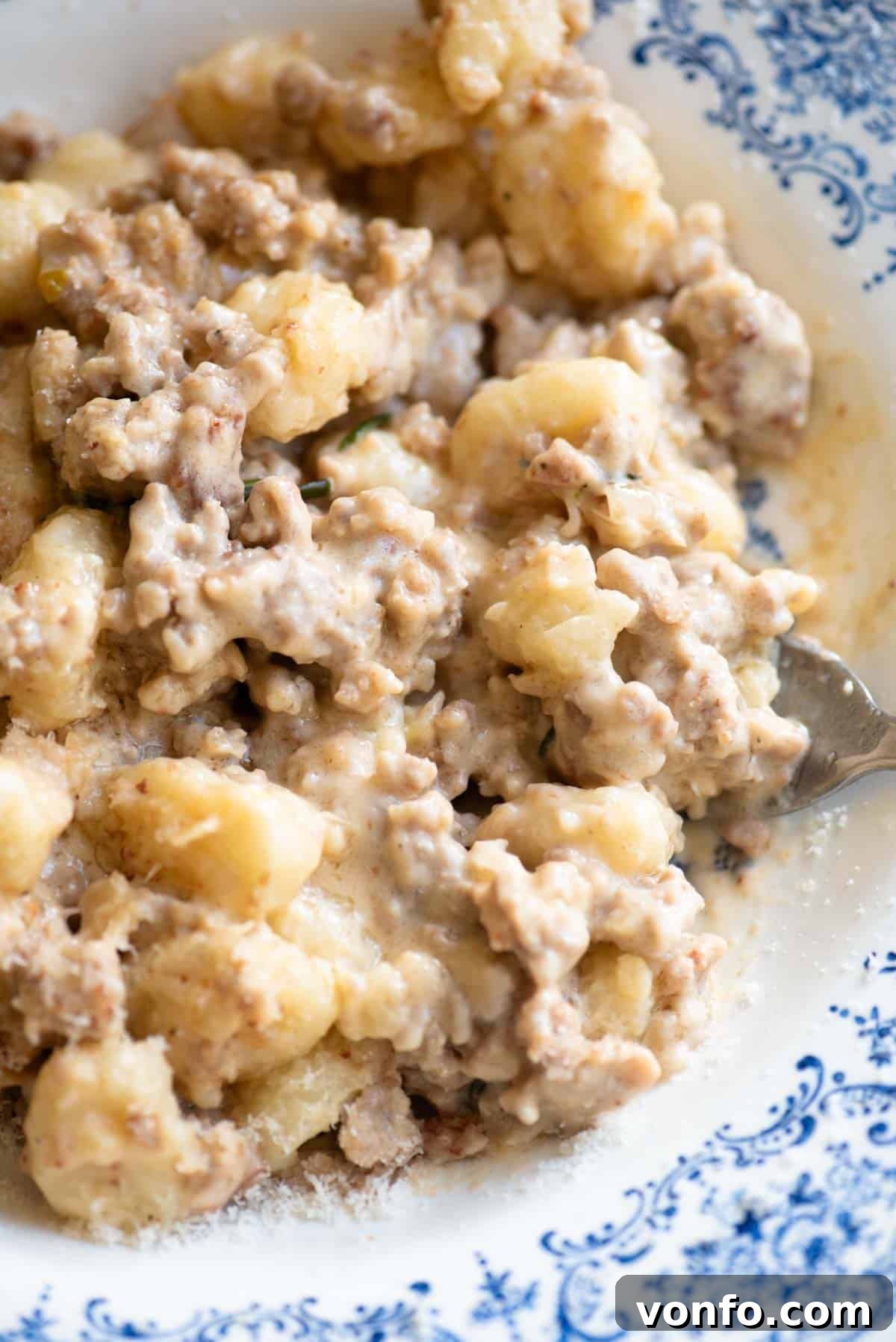 A close-up shot revealing the creamy texture of the white sausage ragu clinging to the soft gnocchi, garnished with fresh rosemary.
