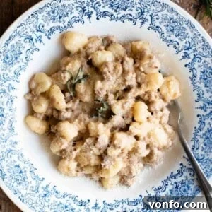 A close-up of gnocchi with a creamy white sausage sauce, beautifully garnished with fresh rosemary.