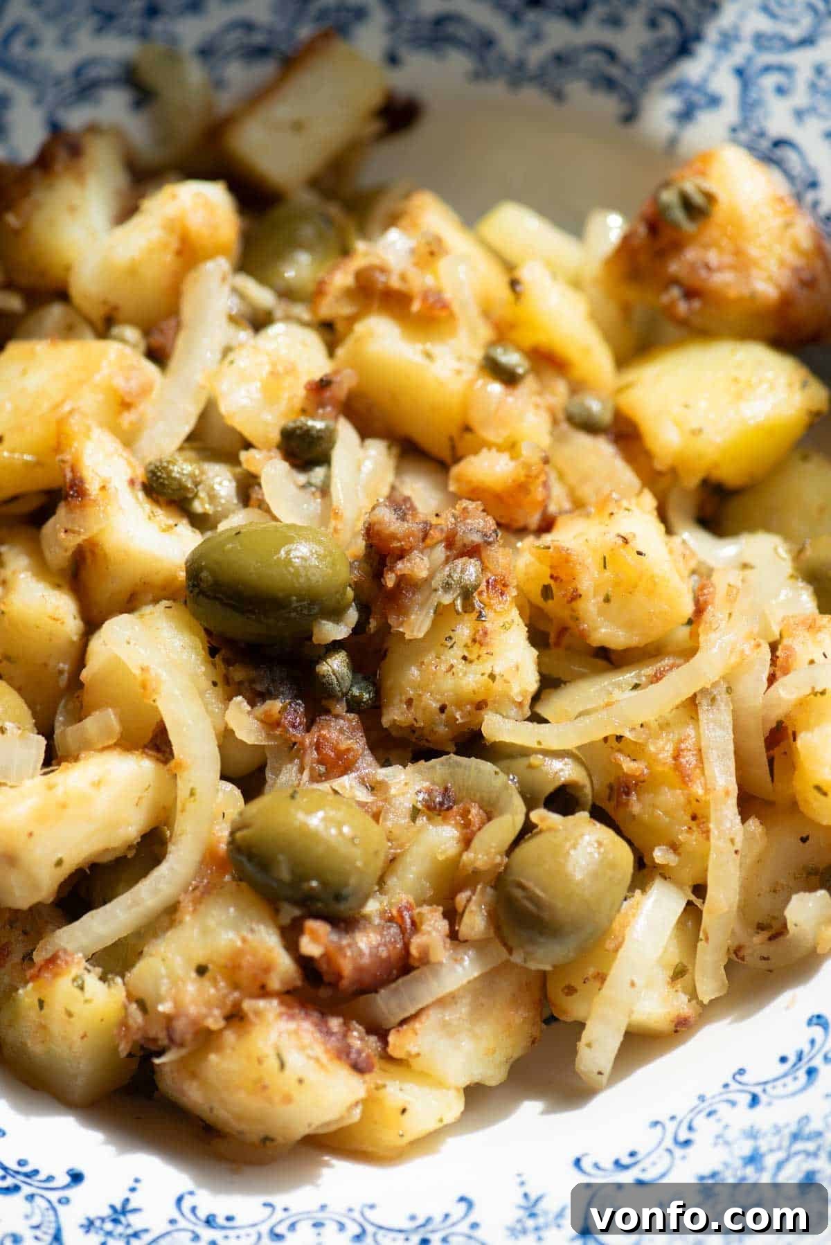 A close-up shot of the finished Patate Apparecchiate dish with olives, capers, and dried oregano visible, highlighting the texture and vibrant ingredients.