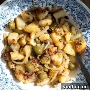 A close up of Sicilian potatoes in a blue bowl with capers and olives, illustrating the final dish.