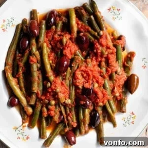 Zesty Green Beans with Olives and Capers 5 A close up of green beans in tomato sauce with olives and capers on a white plate, highlighting the rich colors and textures of the Mediterranean side dish.