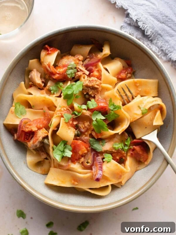 An overhead shot of tuna pasta in a bowl with tomatoes, capers and parsley